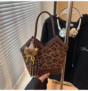 Detail of leopard print handbag with brown leather handle and cute bear charm accessory