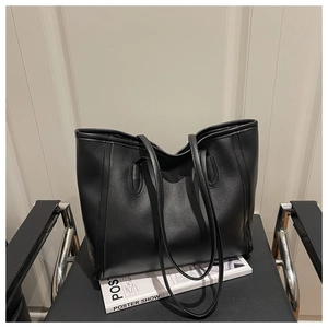 Detail of a minimalist black leather tote bag with stitching on a chair next to a magazine