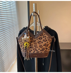 Detail of leopard print handbag featuring leather trim and a cute bear charm accessory