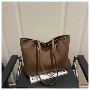 Detailed view of brown leather tote bag with fine texture and slim straps on a chair