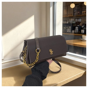 Detail of a brown leather shoulder bag with a gold interlocking clasp in a cafe setting