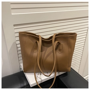 Detail of matte caramel brown leather tote bag with vertical stitching on white books