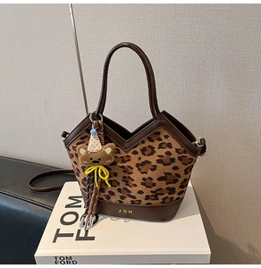 Detail view of leopard print tote bag with brown leather handles and bear charm