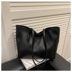 Detail of black leather tote bag showing dual shoulder straps and top handles on a book