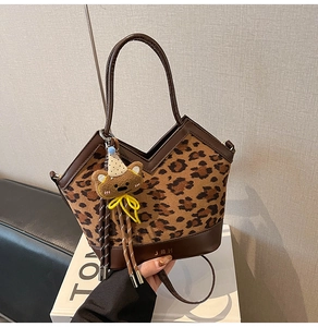Detail of leopard print tote bag with brown leather trim and cute plush bear charm