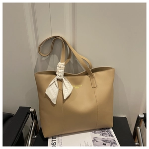Detailed close-up of khaki tote bag with gold logo and decorative geometric silk scarf