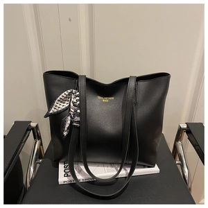 Detail of black faux leather tote with golden logo and decorative geometric silk scarf