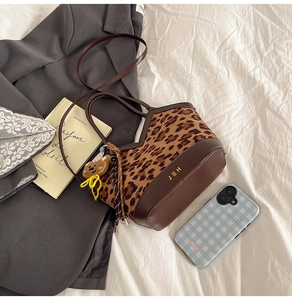 Detail view of leopard print handbag with leather trim and bear pendant on a white sheet