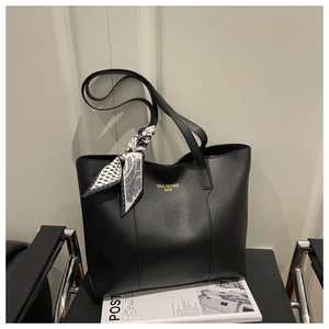 Detail of black leather tote bag featuring a decorative geometric silk scarf on handle
