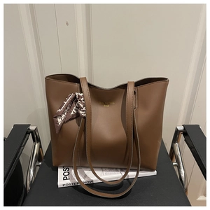 Close-up of brown tote bag featuring golden logo and stylish geometric silk scarf detail