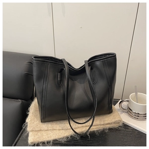 Macro detail of textured black leather tote bag with elegant stitching on a beige surface