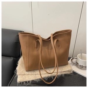 Brown leather tote bag featuring dual handles on a minimalist knit blanket background