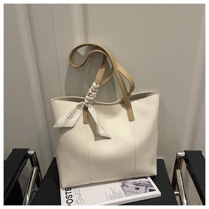 Detail of cream tote bag featuring brown straps, silk scarf accent and gold logo lettering