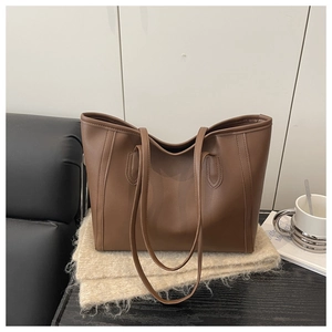 Brown leather tote bag resting on beige knit fabric in a cozy lifestyle setting