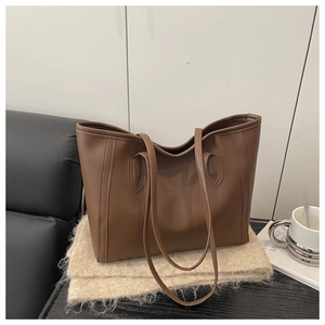 Detail of a brown leather tote bag with slim shoulder straps on a cozy beige scarf