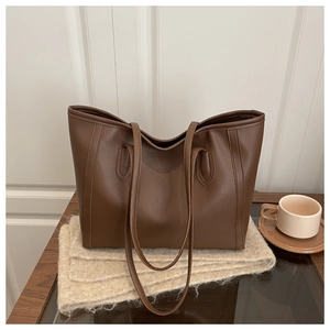 Close-up of brown faux leather tote bag with slender straps on a rustic wooden desk