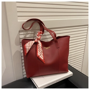 Detail of red tote bag with a silk scarf handle and golden branding on a sofa