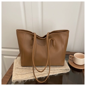 Brown leather tote bag resting on a soft beige wool scarf with a cozy coffee cup