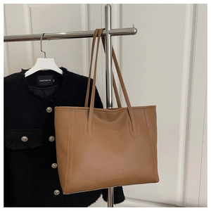 Detail of a brown matte leather tote bag with vertical stitching and long shoulder strap