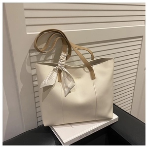 Detail of minimalist cream tote bag with brown handles and elegant silk scarf accessory