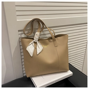 Close-up of beige tote bag with floral silk scarf detail and golden logo on white books
