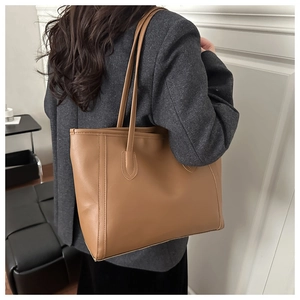 Brown leather tote bag shown on model for size perspective in a minimalist setting