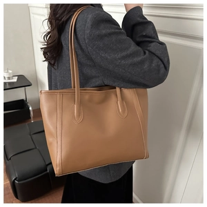 Detailed side view of a textured brown leather tote bag worn as a shoulder bag