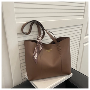 Detail of a brown leather tote bag with gold logo and stylish geometric silk scarf