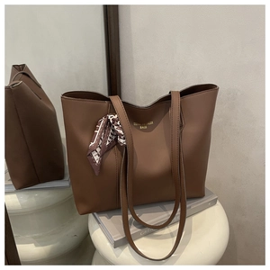 Detailed view of brown leather tote bag with silk scarf charm and gold logo on white stand