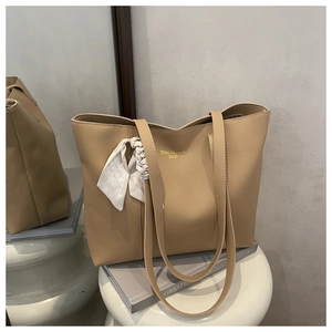 Macro shot of khaki large tote bag with decorative silk scarf on handle and gold logo