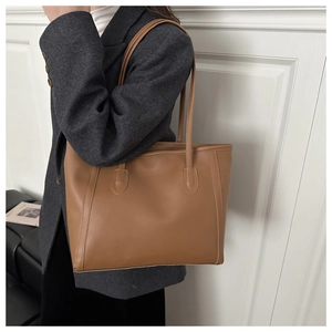 Brown leather tote bag shown on shoulder of a model to display size and drape details