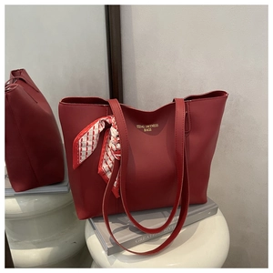 Close-up of burgundy leather tote bag featuring elegant silk scarf and embossed text logo