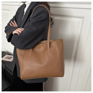 Detail of caramel minimalist tote bag on a sofa showing premium leather texture