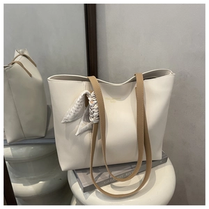 Detail of creamy tote bag with brown handles and a stylish patterned scarf accent