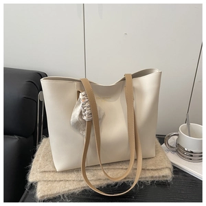 Detail of cream tote bag featuring a decorative silk scarf and brand logo engraving