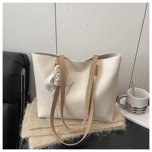 Detail of off-white leather tote bag featuring a decorative silk scarf and golden lettering