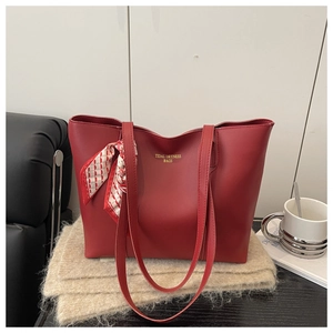Detail of red leather tote bag with silk scarf and gold lettering on black tabletop