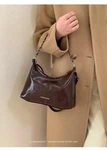 Close-up of brown waxed leather shoulder bag with metal chain strap and logo detail
