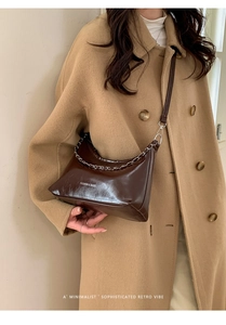 Dettaglio di una borsa hobo marrone scuro con catena d'argento, indossata su un cappotto kaki