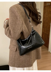 Dettaglio borsa hobo in pelle nera lucida con catena argento su giacca in tweed