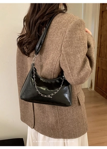 Elegante borsa a spalla nera lucida con dettaglio catena argento su blazer minimal