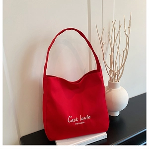 Close-up of red canvas tote bag with white C'est la vie text and brand logo detail