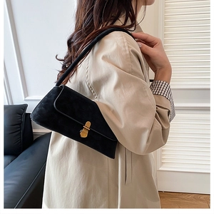 Dettaglio borsa a tracolla in pelle scamosciata nera con chiusura dorata su trench beige