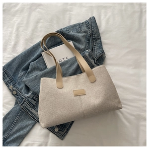 Close-up of beige canvas tote bag with brown leather handles and decorative patch detail