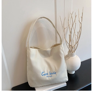 Close-up of cream canvas tote bag with blue C'est la vie print on a minimalist desk