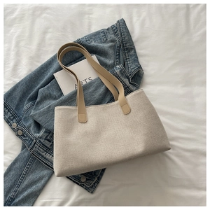 Detail of beige canvas tote bag with brown leather handles on white fabric background
