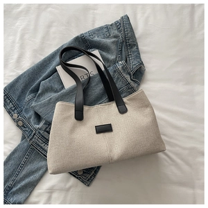 Close-up of beige canvas tote bag with black handles on a white fabric surface