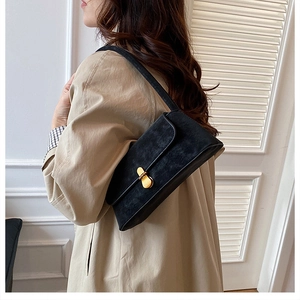 Dettaglio borsa a spalla in camoscio nero con fibbia dorata indossata su trench coat