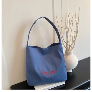 Detailed view of dark blue tote bag with red C'est lavie embroidery in a minimalist setting