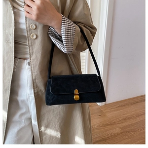 Dettaglio della borsa baguette nera con fibbia dorata indossata con un trench beige